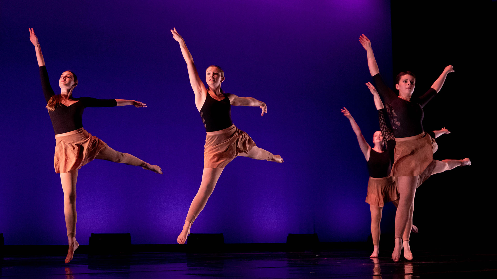 Students in black dance outfits performing against a blue and purple backdrop