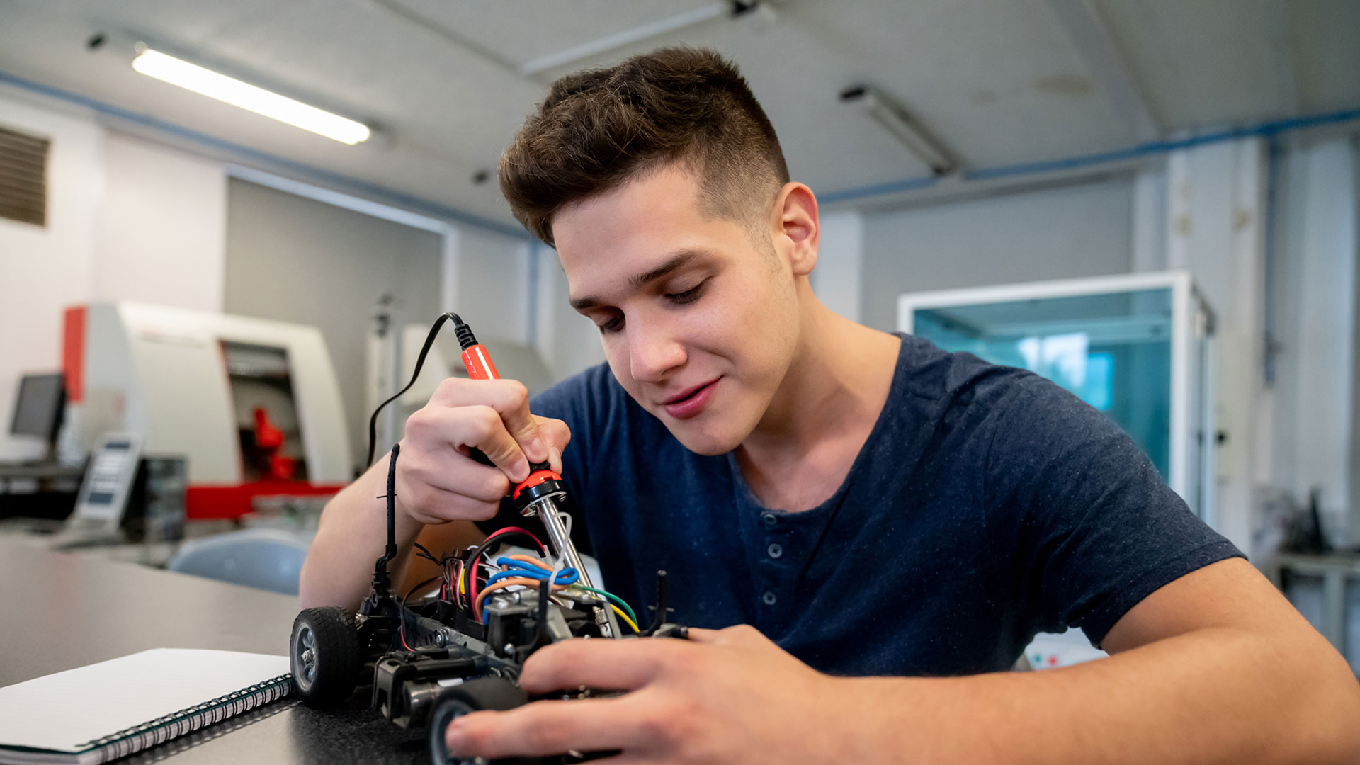 A student works on the wiring on a robot in a classroom