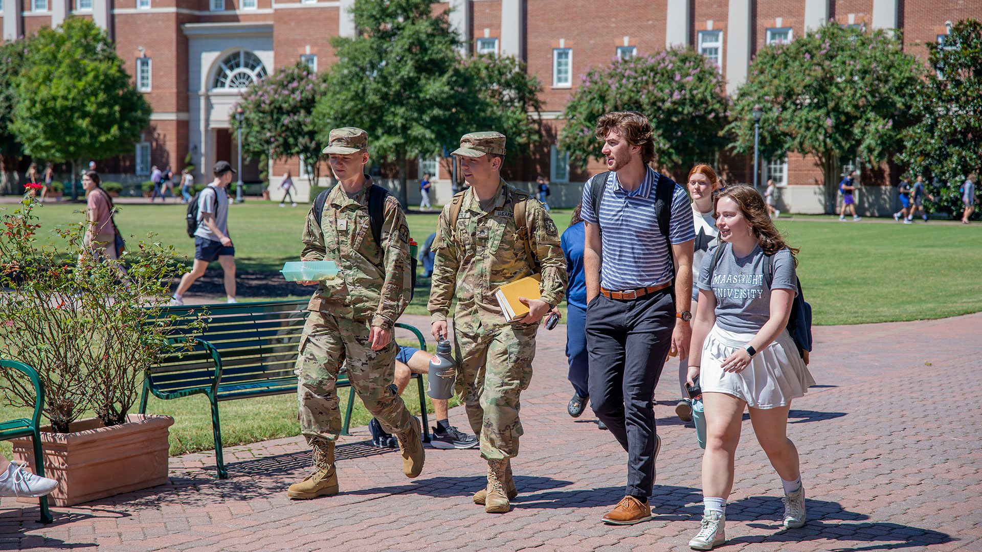  Two Army ROTC cadets in uniform walk with two college students on a sunny campus.