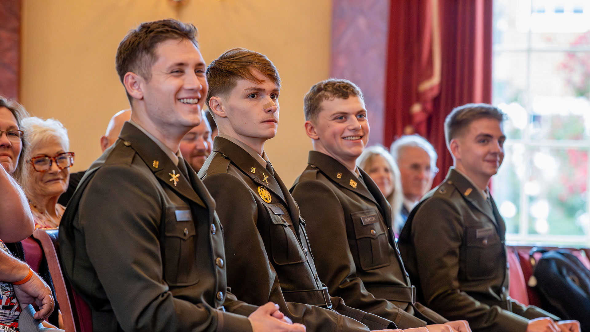 Four newly commissioned Army ROTC second lieutenants in uniform are seated and smiling during their commissioning ceremony.