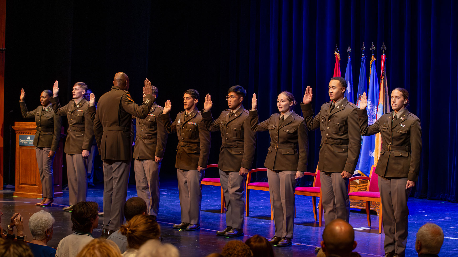 A line of newly commissioned Army ROTC second lieutenants in uniform raise their right hands to take the oath on a stage.