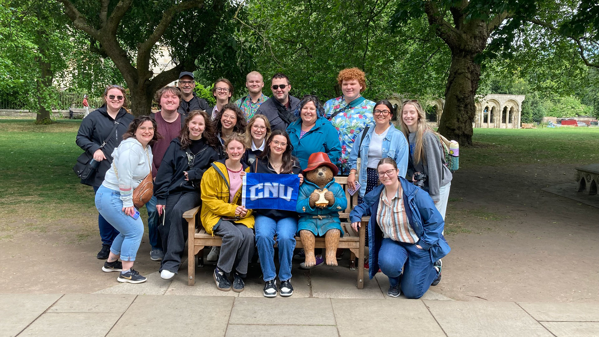 A group of college students with their professor sit on a bench with Paddington Bear.