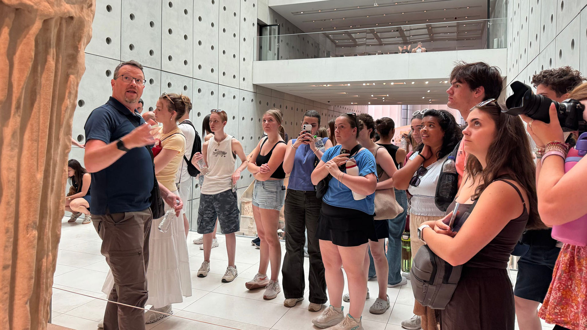 A professor addresses students in front of a statue in a museum