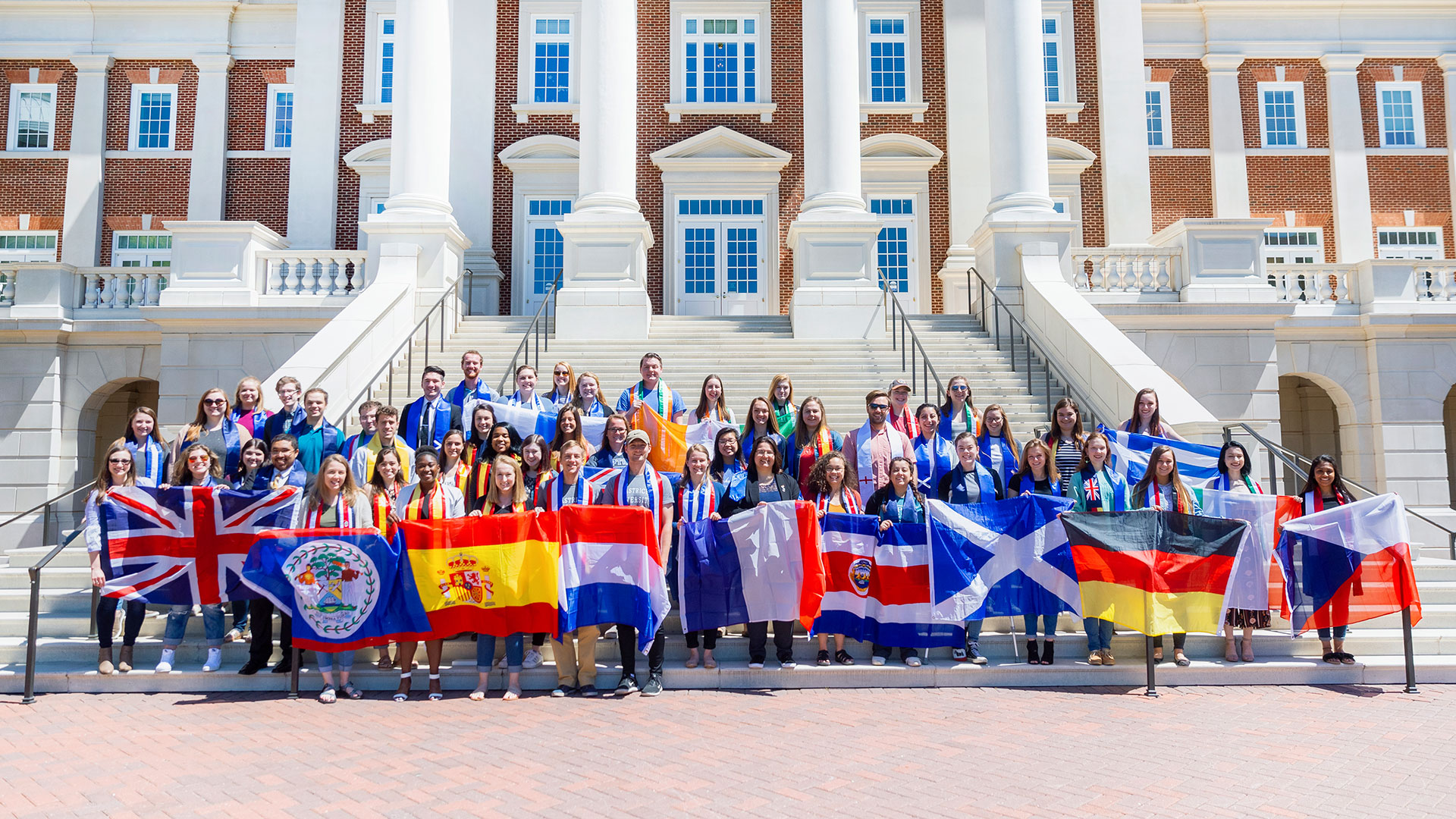 Study abroad students stand on the steps of CNH and hold flags from the country they visited