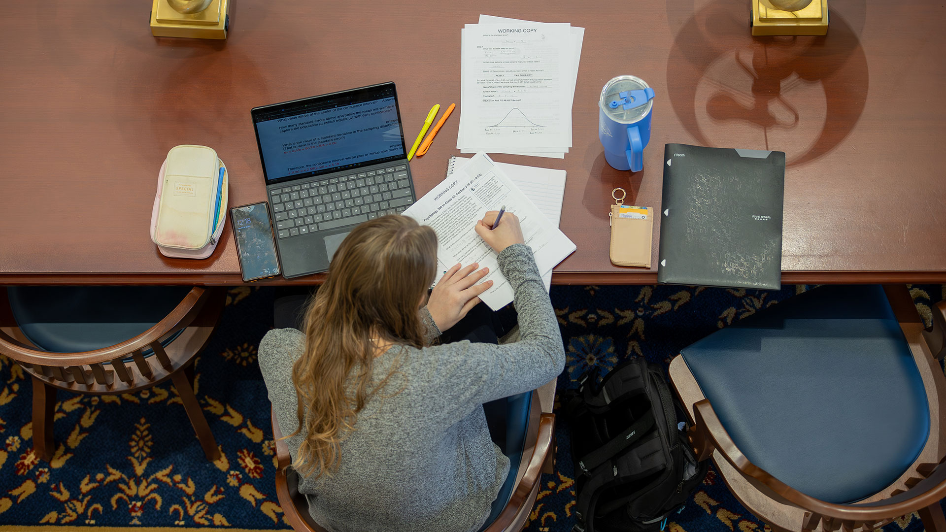 Overhead shot of a student sitting at a table in the library reading room with a laptop and notes spread out