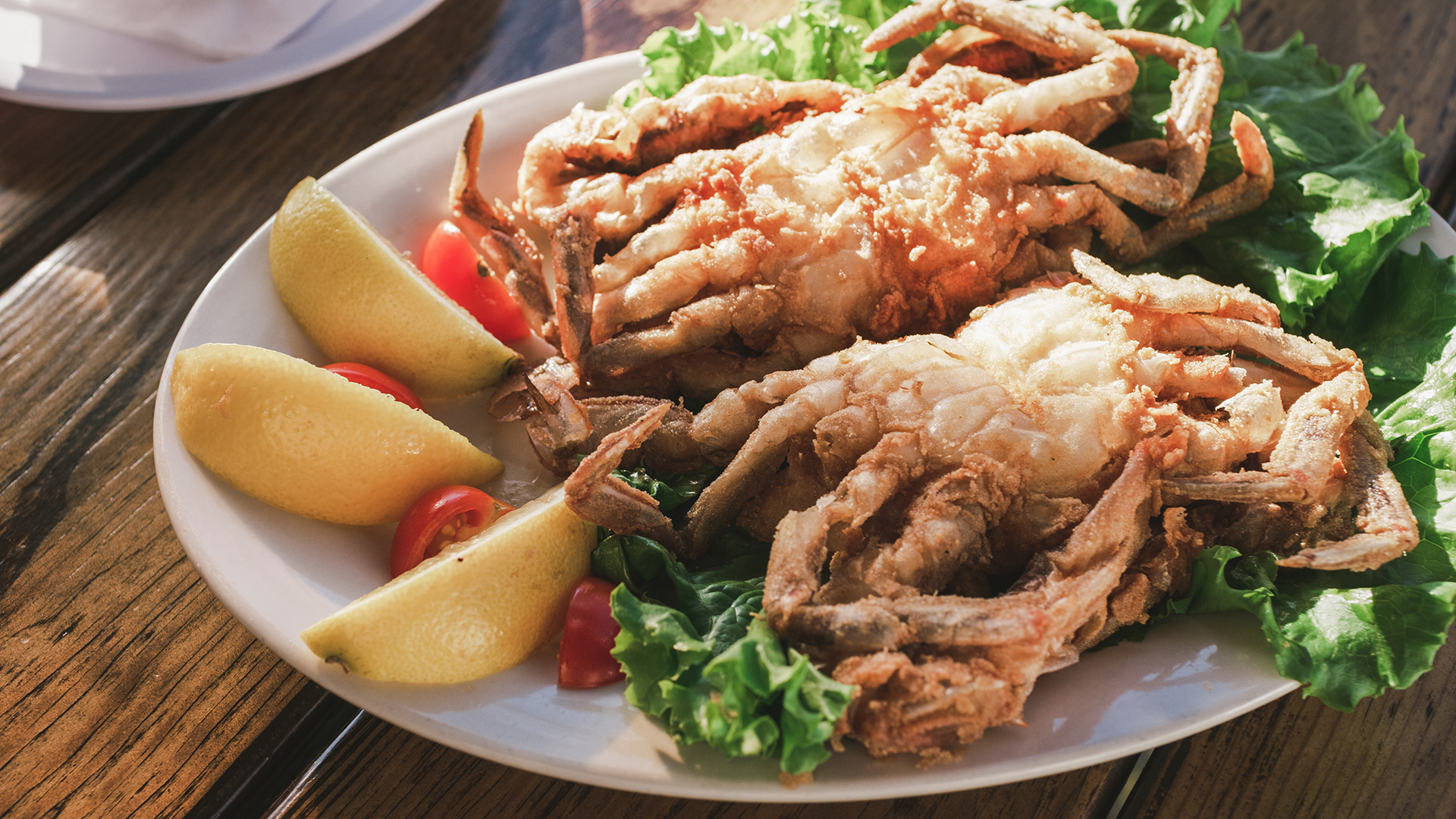 Two cooked softshell crabs on a plate with lemon slices